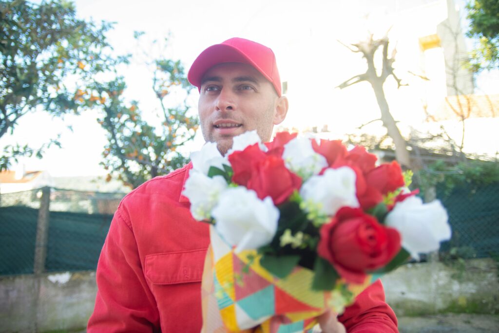 Florist in red attire delivering a colorful bouquet outdoors on a sunny day.